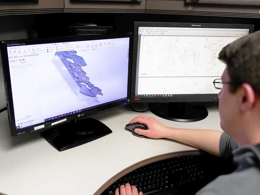 Engineer working at a dual-monitor workstation with model displayed on one screen and technical drawings on the other.